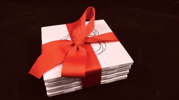 Image of engraved white coasters with decorative heart design bundled with red ribbons - Donley Woodworking